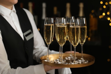 Waiter holding tray with glasses of champagne on blurred background, closeup