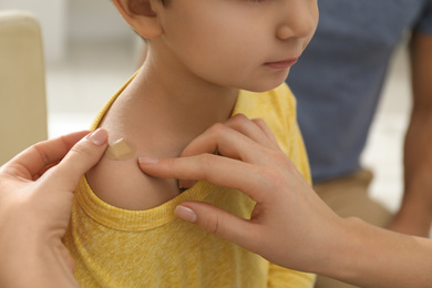 Photo of Mother putting sticking plaster onto son's shoulder indoors, closeup