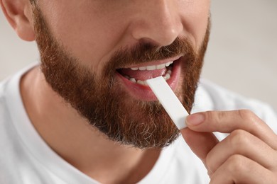 Man putting chewing gum into mouth on blurred background, closeup