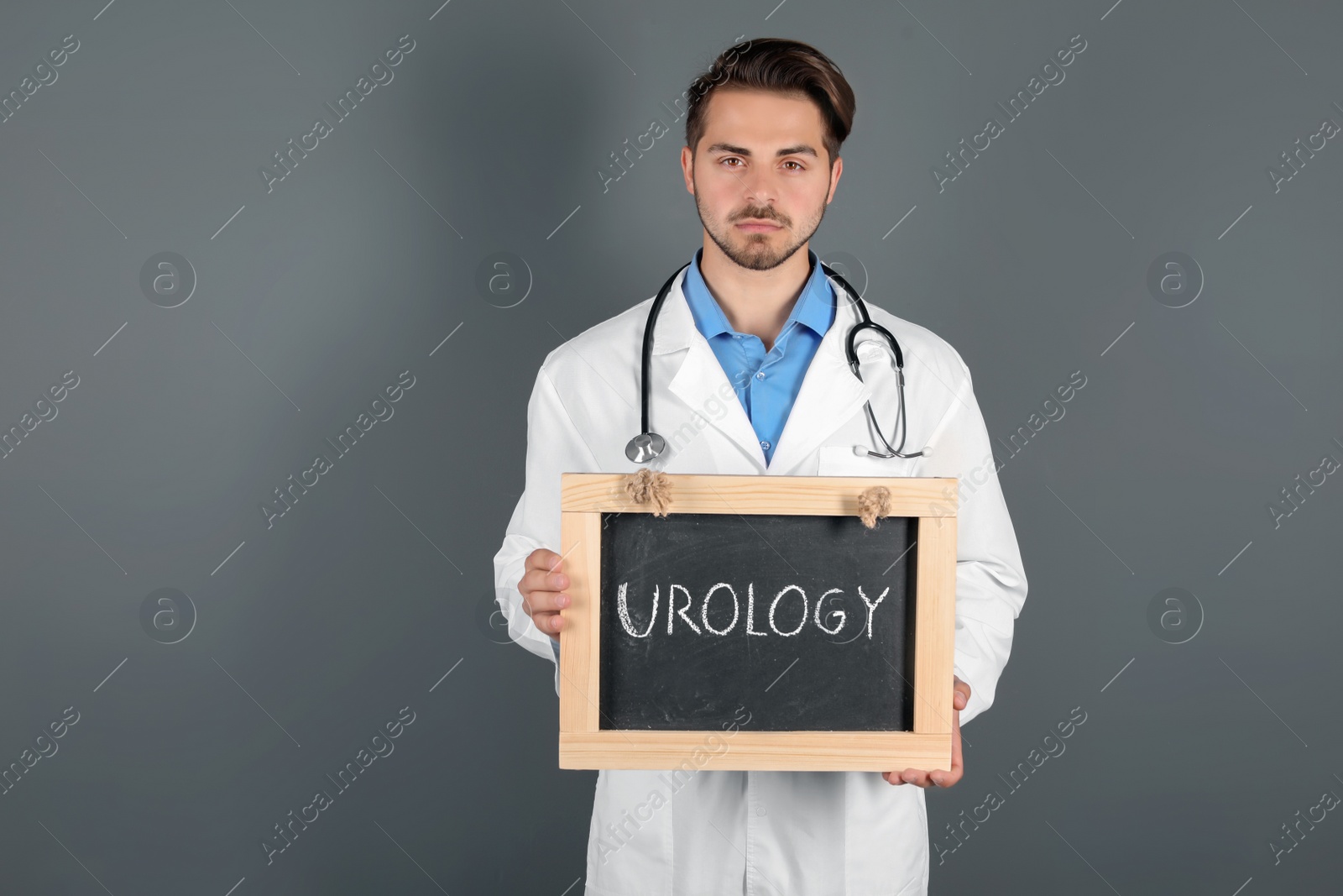 Photo of Male doctor holding chalkboard with word UROLOGY on grey background