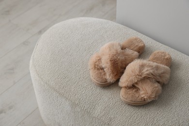 Photo of Soft beige slippers on ottoman in room, space for text