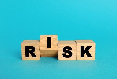 Photo of Word Risk made of wooden cubes on turquoise background