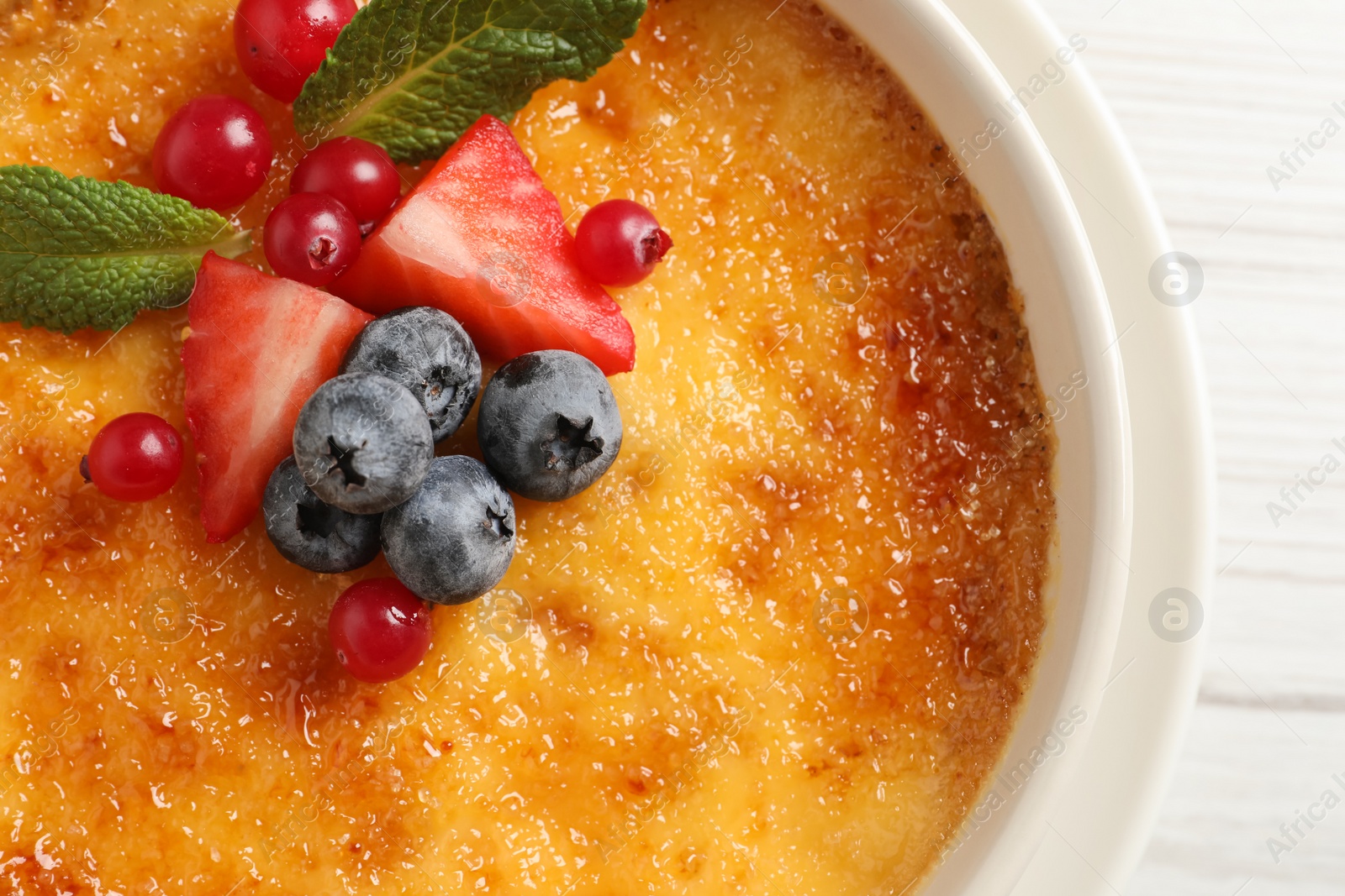 Photo of Delicious creme brulee with fresh berries on white wooden table, closeup