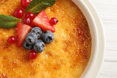 Photo of Delicious creme brulee with fresh berries on white wooden table, closeup