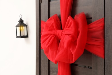 Photo of Wooden door with beautiful red bow and lantern hanging on wall. Christmas decoration