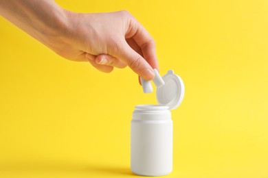 Photo of Woman taking chewing gums from jar on yellow background, closeup