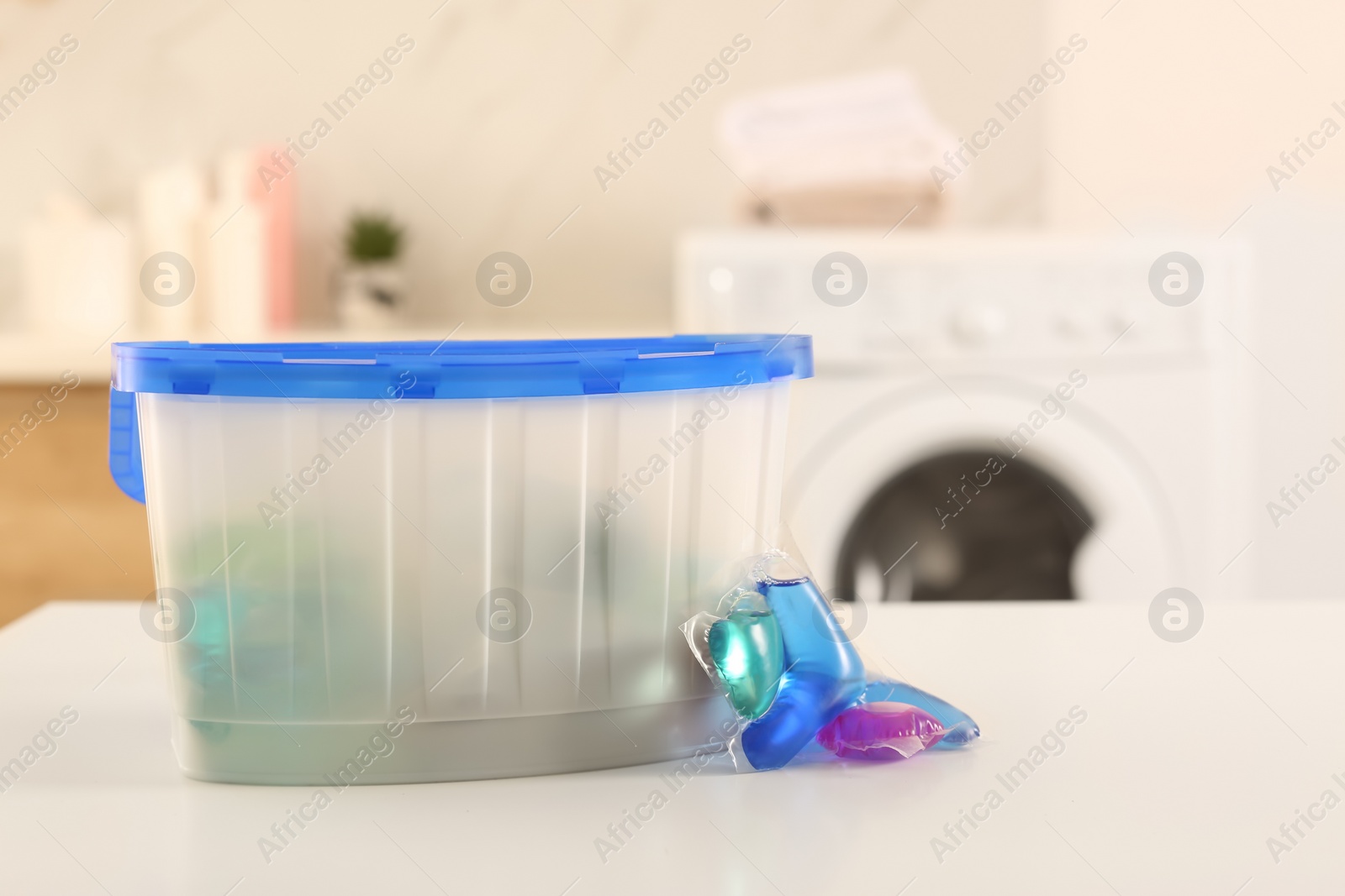 Photo of Laundry container and washing detergent capsules on table indoors