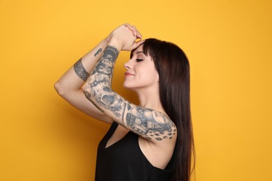 Photo of Beautiful woman with tattoos on arms against yellow background