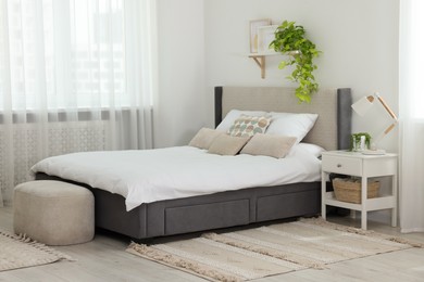 Photo of Stylish bedroom interior with large comfortable bed, ottoman and bedside table
