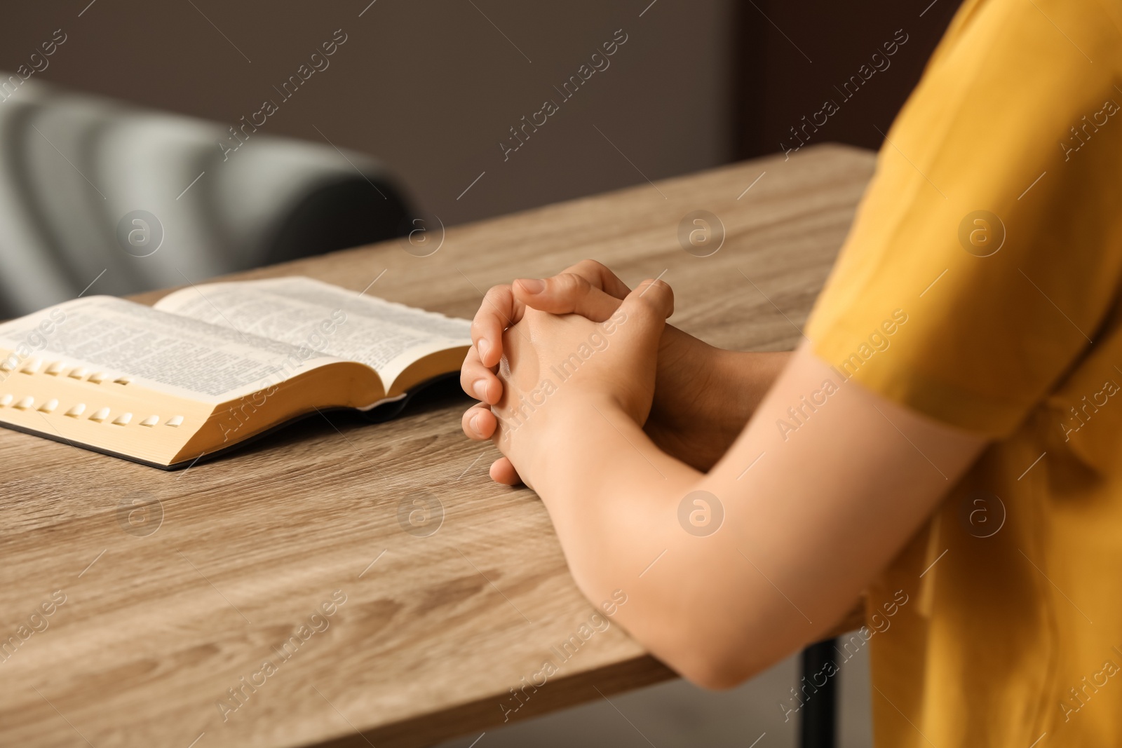 Photo of Religious woman praying over Bible at wooden table indoors, closeup