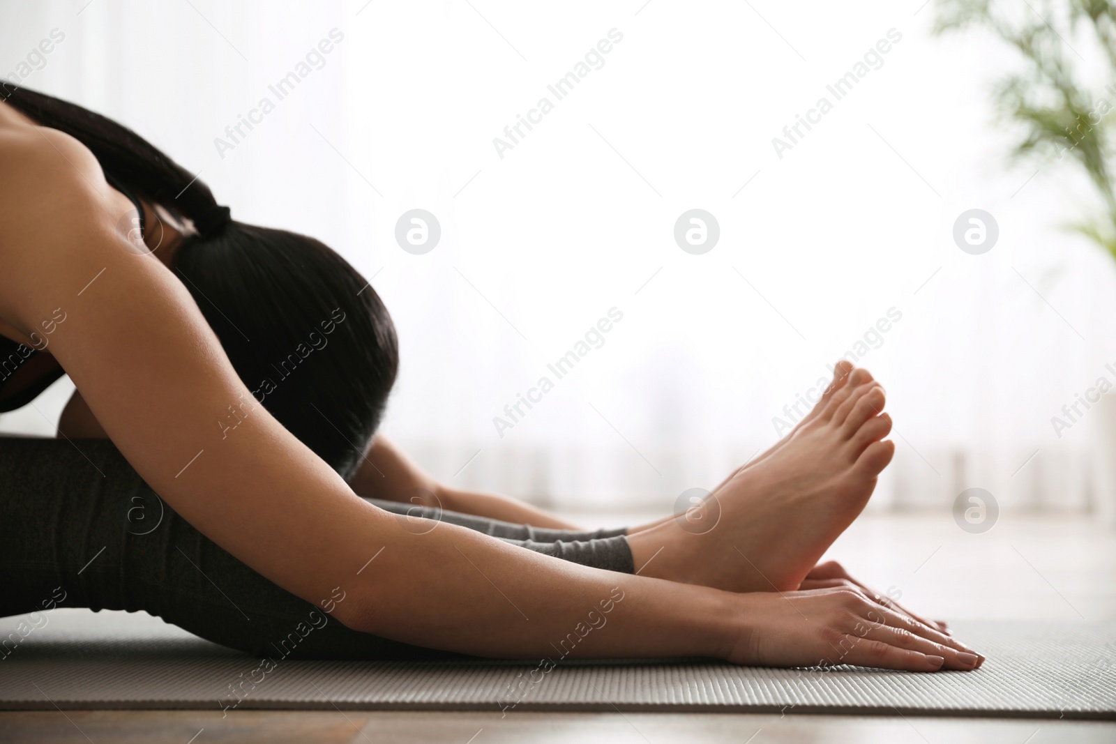 Photo of Young woman practicing seated forward bend asana in yoga studio, closeup. Paschimottanasana pose