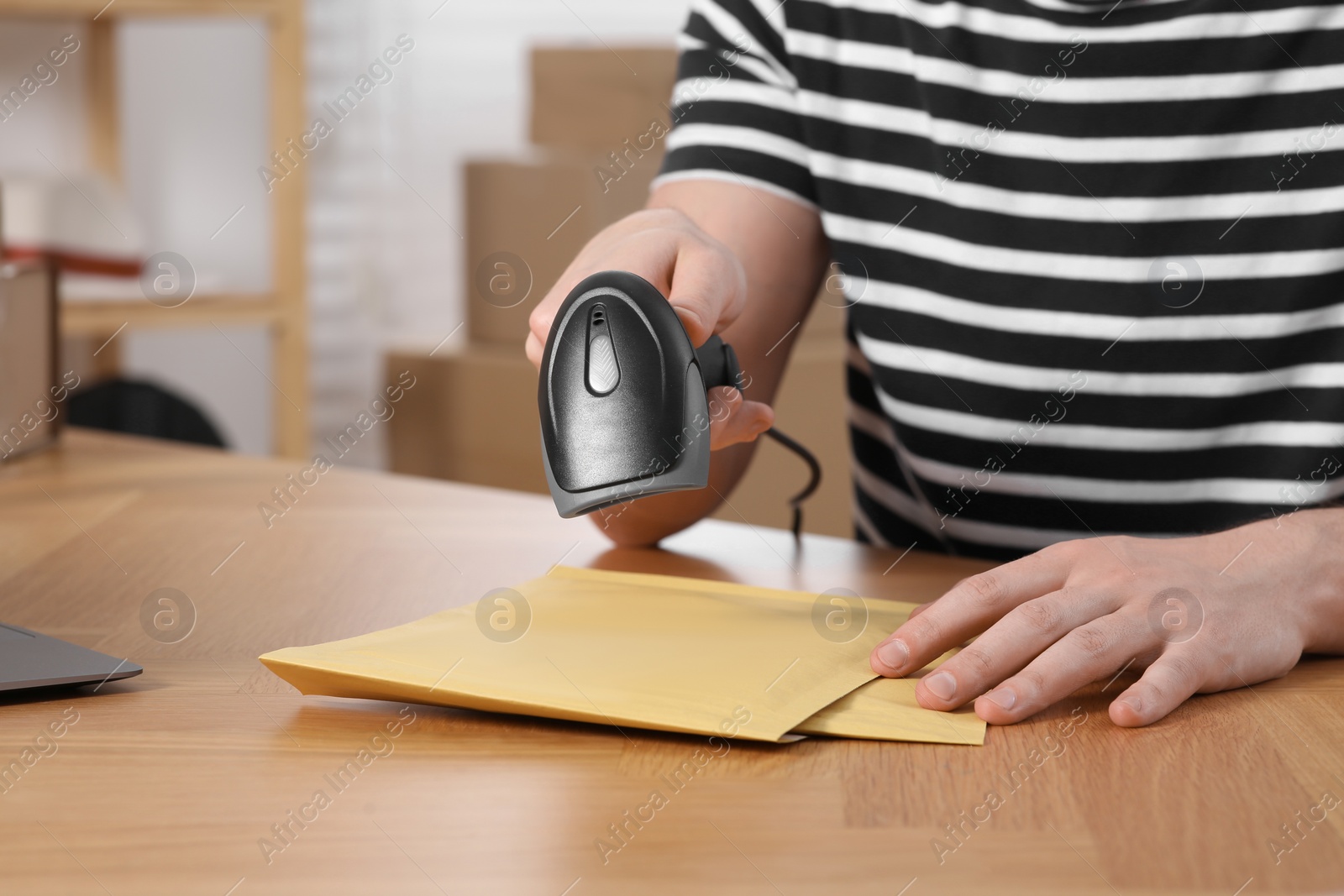 Photo of Seller with scanner reading parcel barcode at table in office, closeup. Online store