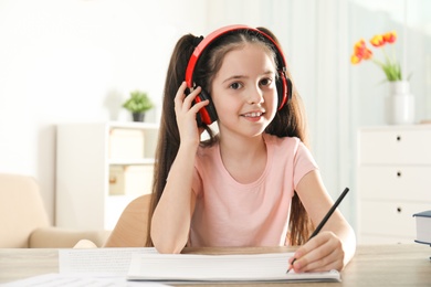 Little girl writing music notes at table indoors