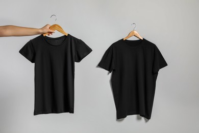 Photo of Woman holding hanger with t-shirt near another one on light wall, closeup. Mockup for design
