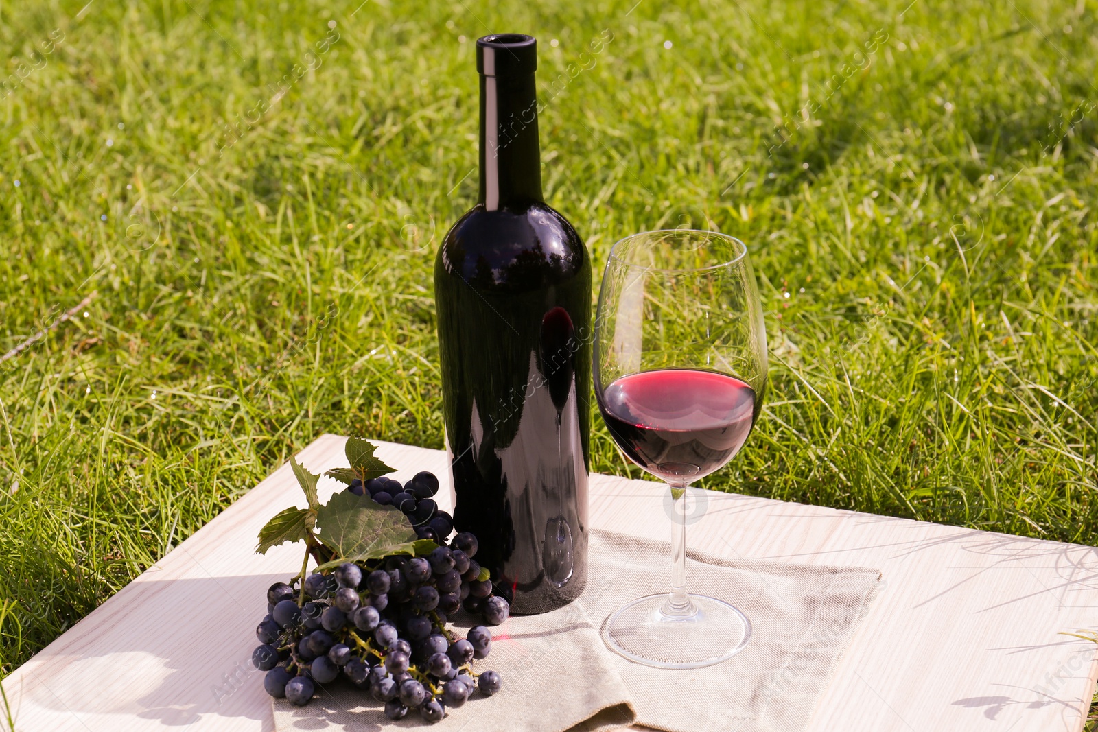 Photo of Red wine and delicious grapes served on green grass outdoors