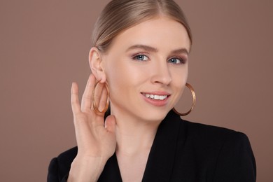 Beautiful young woman with elegant earrings on light brown background