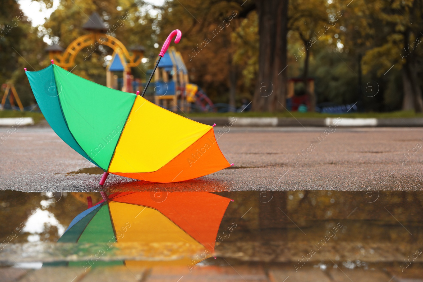 Photo of Colorful umbrella near puddle outdoors, space for text