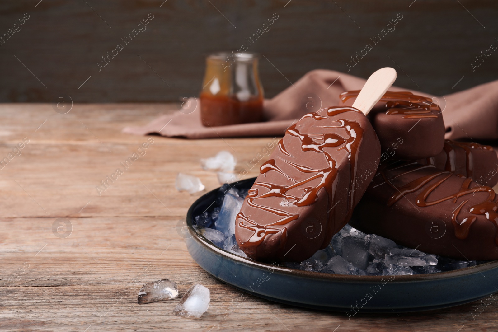 Photo of Delicious glazed ice cream bars and ice cubes on wooden table. Space for text