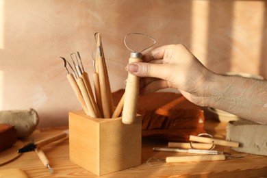 Photo of Clay crafting tools. Woman with wooden loop holder in workshop, closeup