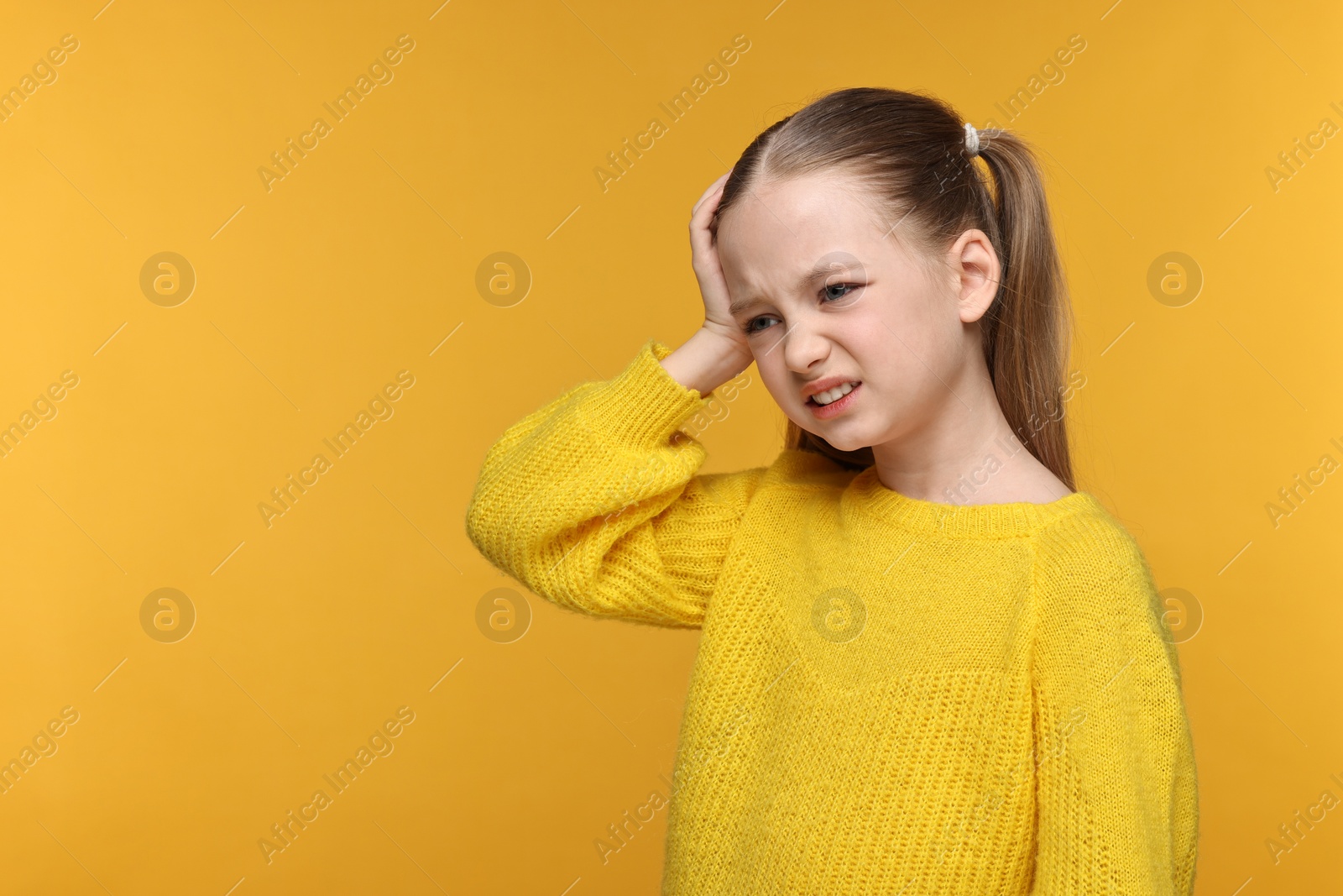 Photo of Little girl suffering from headache on yellow background. Space for text