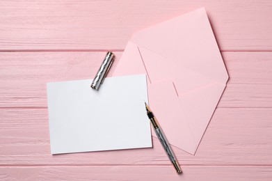 Photo of Blank sheet of paper, pen and letter envelope on pink wooden table, top view. Space for text