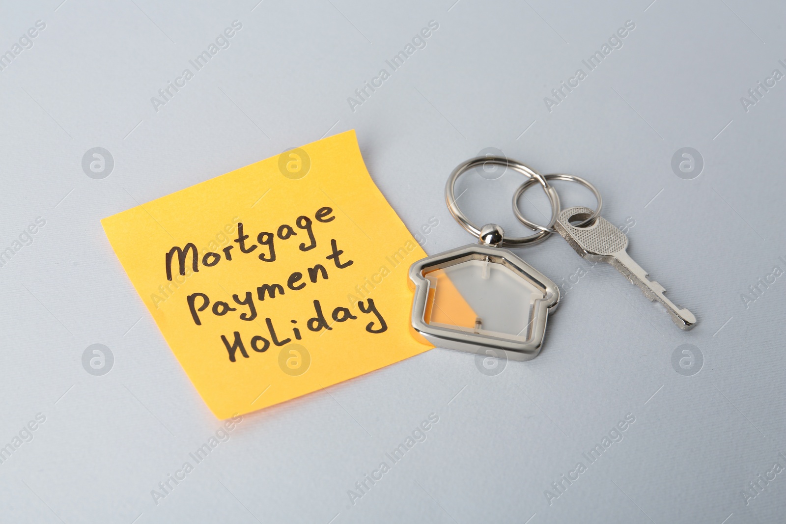 Photo of Key with trinket in shape of house and phrase Mortgage payment holiday written on sticky note against light grey background