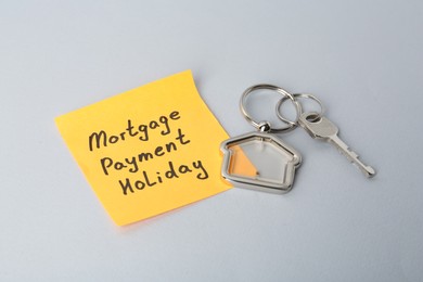 Photo of Key with trinket in shape of house and phrase Mortgage payment holiday written on sticky note against light grey background