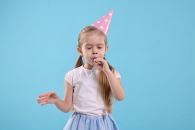 Photo of Birthday celebration. Cute little girl in party hat with blower on light blue background