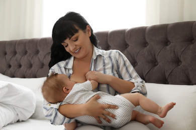 Photo of Woman breastfeeding her little baby on bed indoors