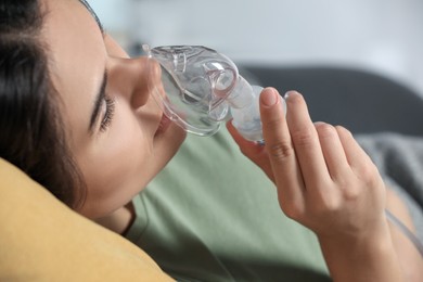 Photo of Sick young woman using nebulizer at home, closeup