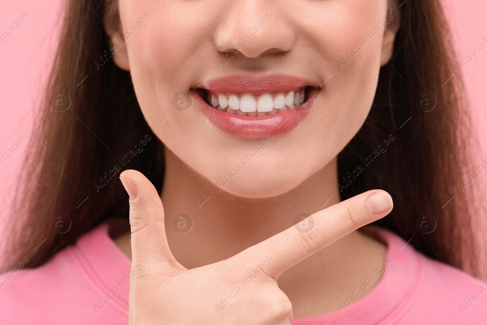 Photo of Beautiful woman showing her clean teeth and smiling on pink background, closeup