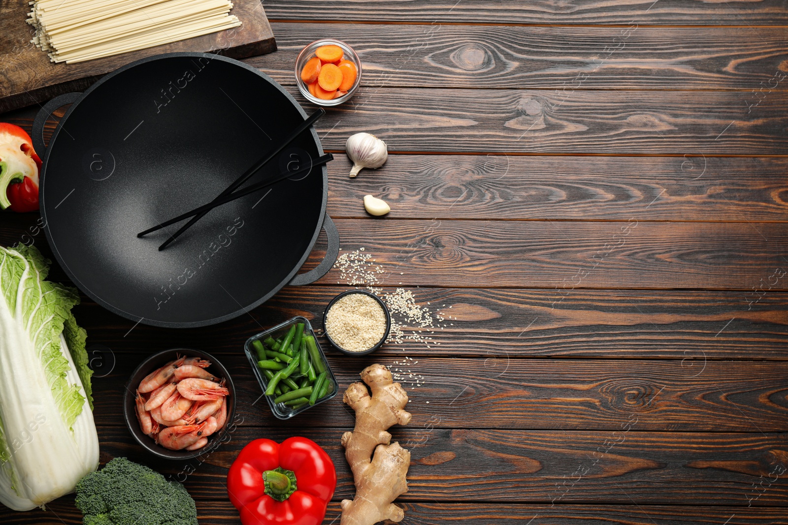 Photo of Empty iron wok with chopsticks and raw ingredients on wooden table, flat lay. Space for text