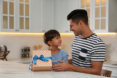 Photo of Man receiving gift for Father's Day from his son in kitchen