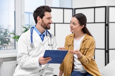 Photo of Doctor with clipboard consulting patient during appointment in clinic