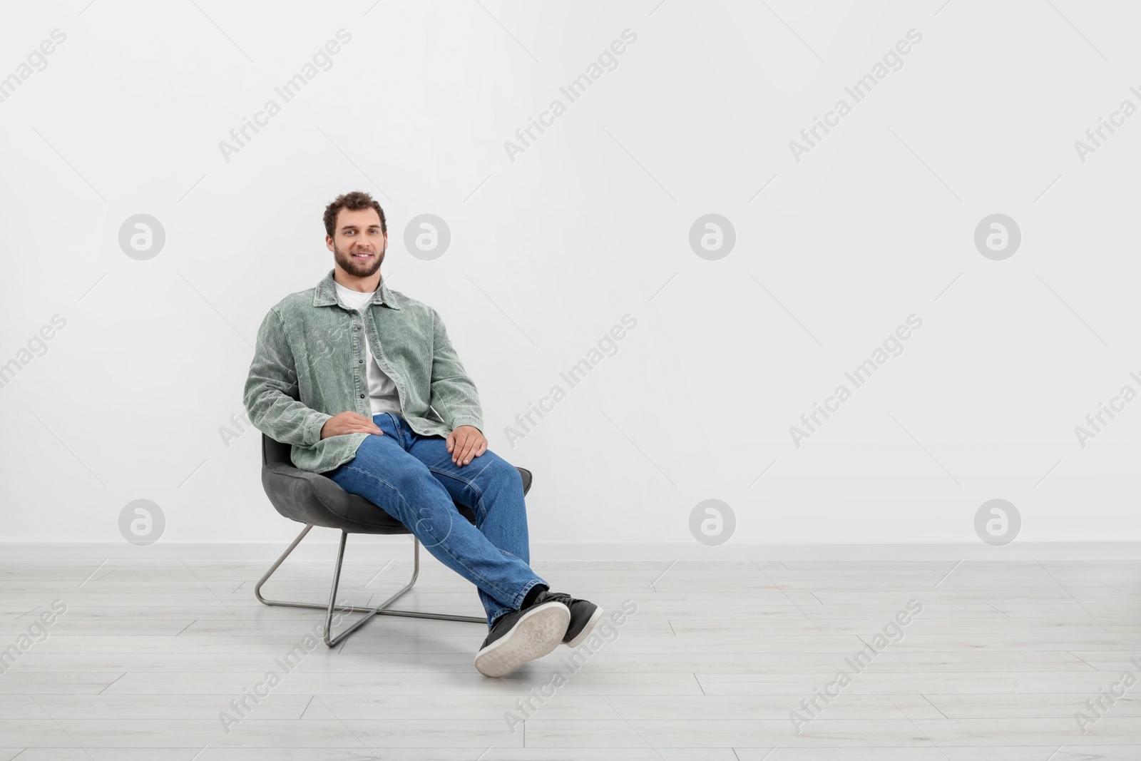 Photo of Young man sitting on comfortable chair indoors. Space for text