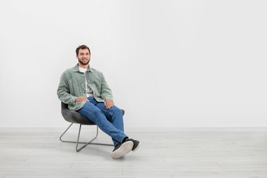 Young man sitting on comfortable chair indoors. Space for text