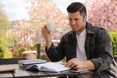 Happy man with headphones reading book in outdoor cafe