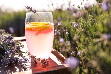 Photo of Glass of fresh lemonade on wooden tray in lavender field. Space for text