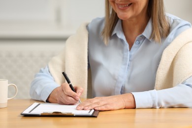 Photo of Smiling senior woman signing Last Will and Testament at table indoors, closeup