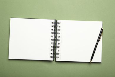 Photo of Stylish open notebook and pen on green background, top view
