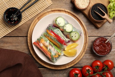 Photo of Delicious rolls wrapped in rice paper on wooden table, flat lay