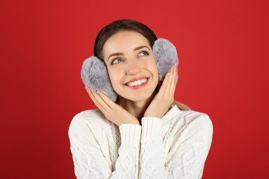 Photo of Happy woman wearing warm earmuffs on red background