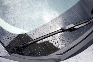 Car wiper cleaning water drops from windshield glass, closeup
