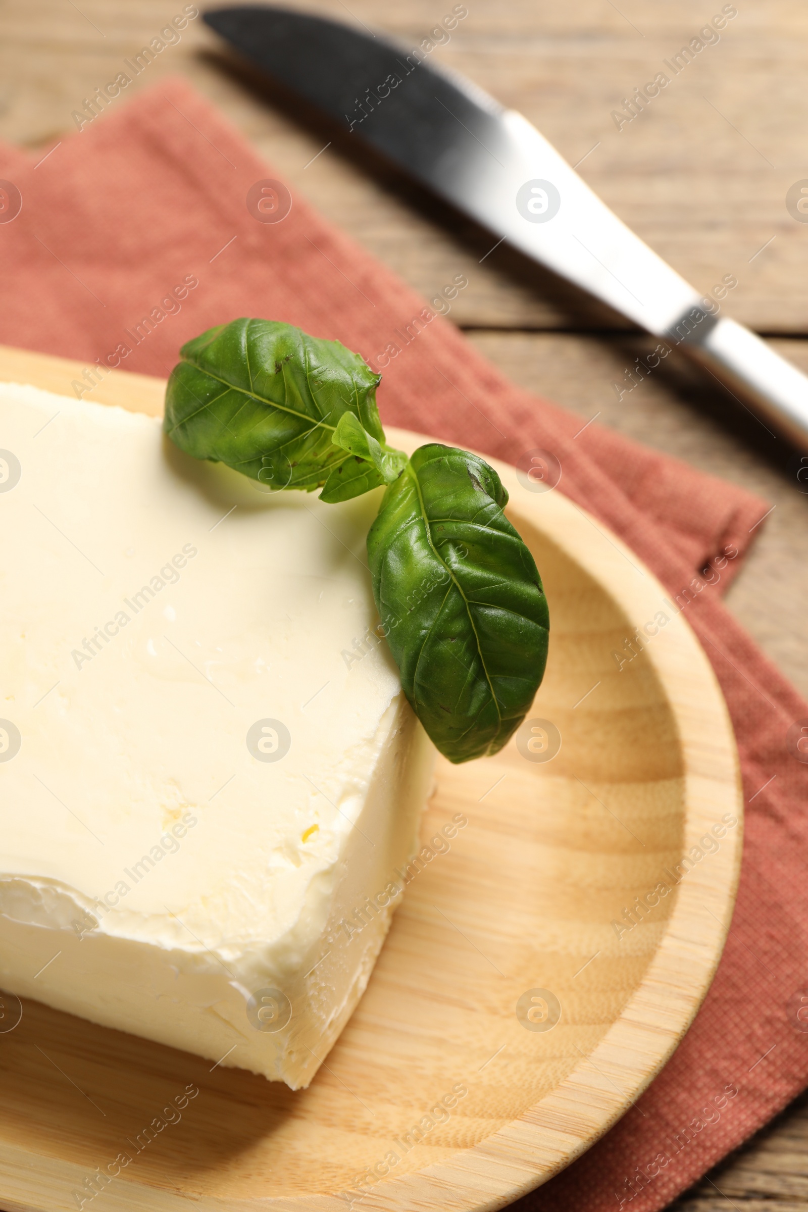 Photo of Block of tasty butter with basil and knife on wooden table, closeup