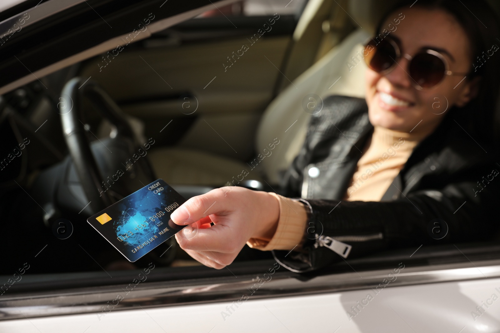 Photo of Woman sitting in car and giving credit card at gas station, focus on hand