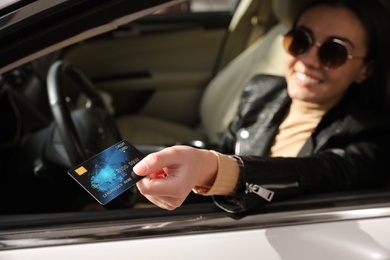 Woman sitting in car and giving credit card at gas station, focus on hand