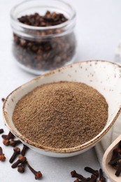 Aromatic clove powder and dried buds on light table, closeup