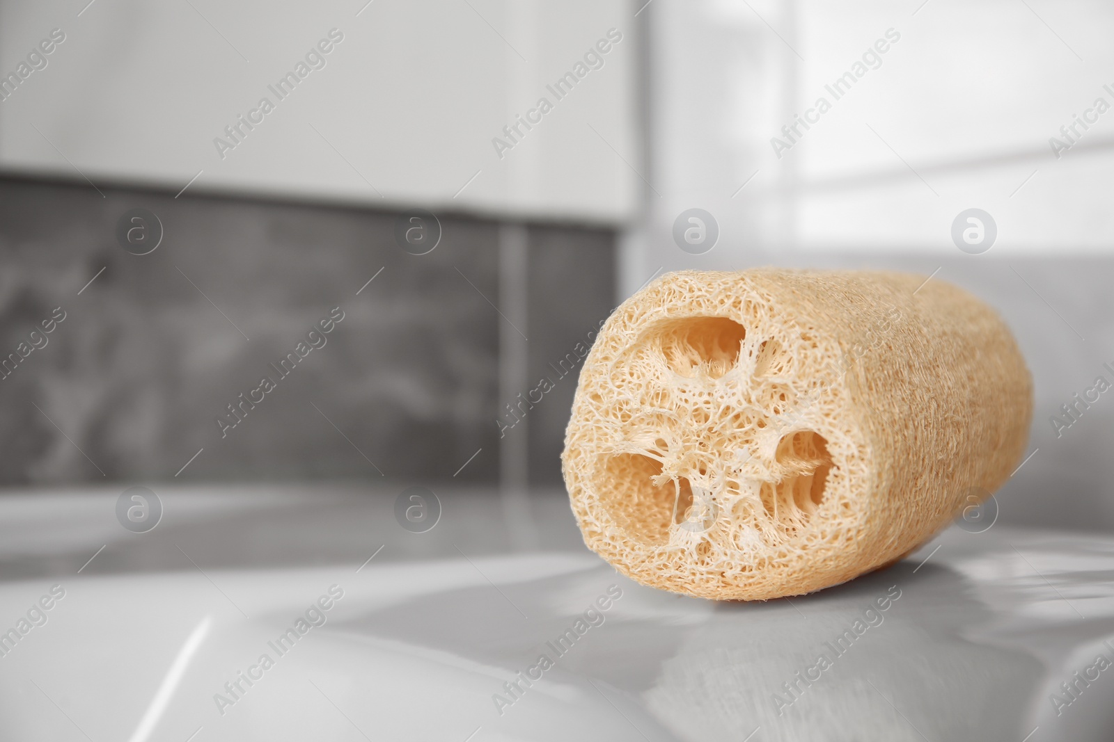 Photo of Natural loofah sponge on washbasin in bathroom, closeup. Space for text