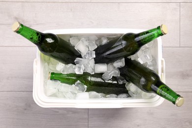 Photo of Plastic cool box with ice cubes and beer on wooden floor, top view