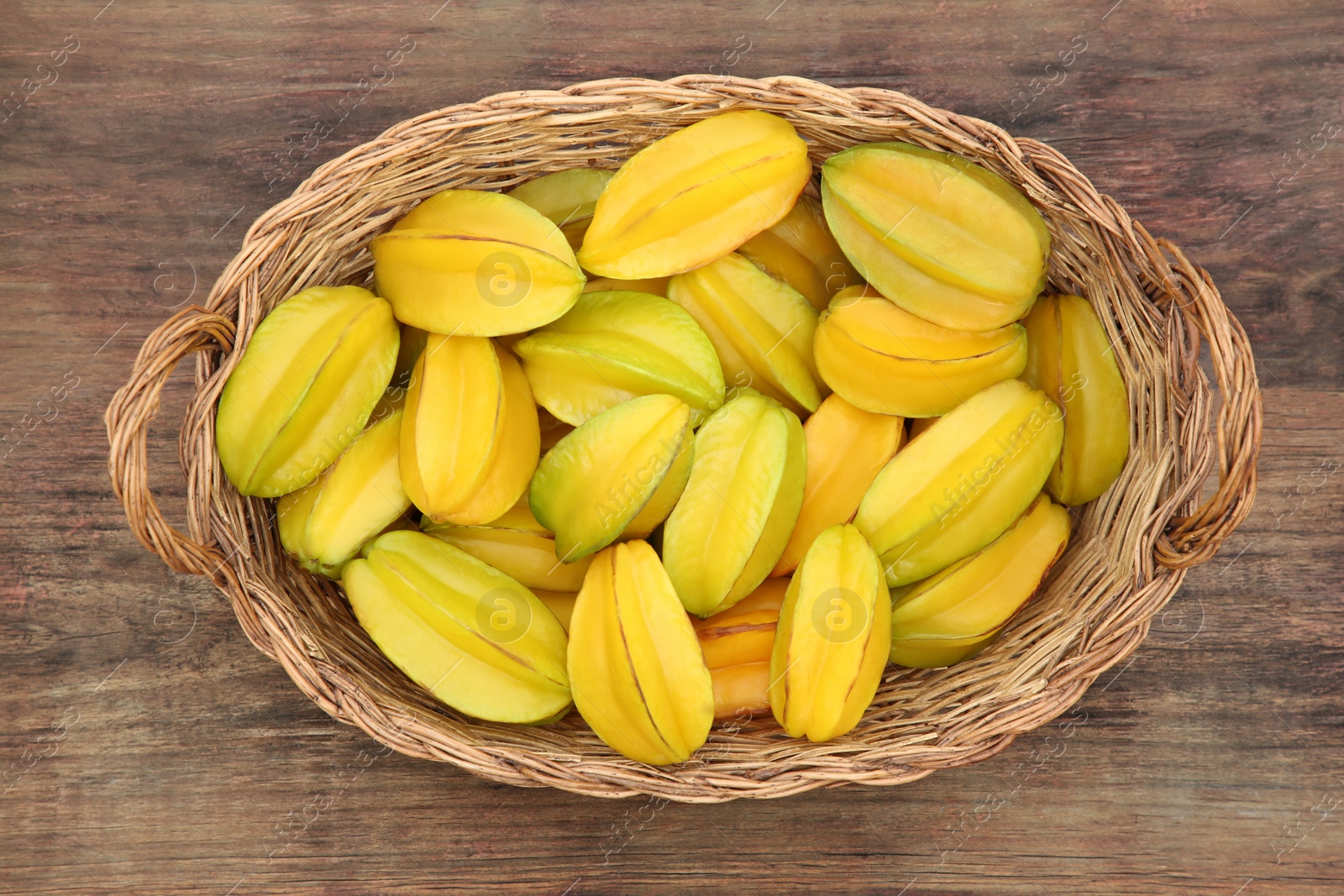 Photo of Delicious ripe carambolas in wicker basket on wooden table, top view